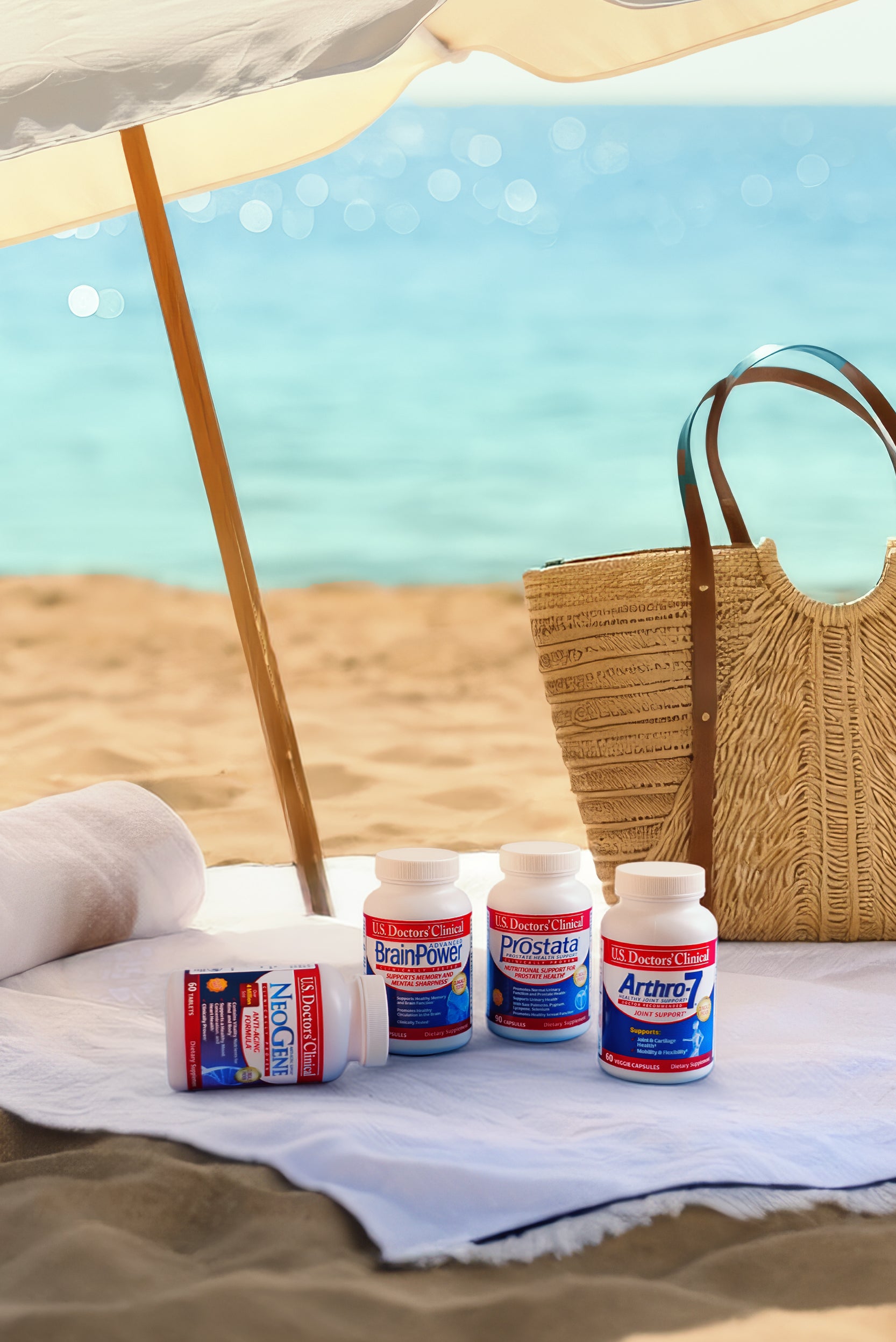 Four dietary supplement bottles branded "U.S. Doctors' Clinical" sit on a white towel spread across a sandy beach. A rolled-up white towel rests nearby, and a large woven wicker tote bag with leather handles stands in the background. The calm, turquoise ocean water is visible under the bright sunlight.